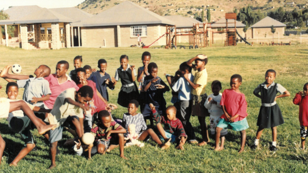 Eine Gruppe von Kindern auf einer Wiese vor einigen Gebäuden