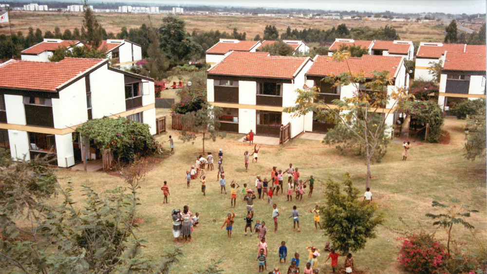 Vogelansicht einiger Häuser und einer Wiese auf der Kinder spielen