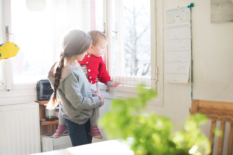 Mädchen schaut mit kleiner Schwester beim Fenster hinaus