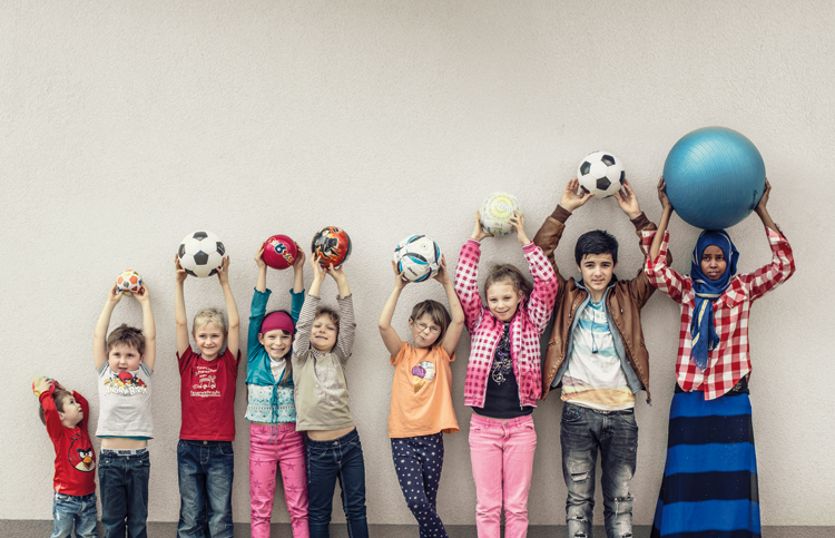 Kinder stehen in einer Reihe und halten Bälle hoch
