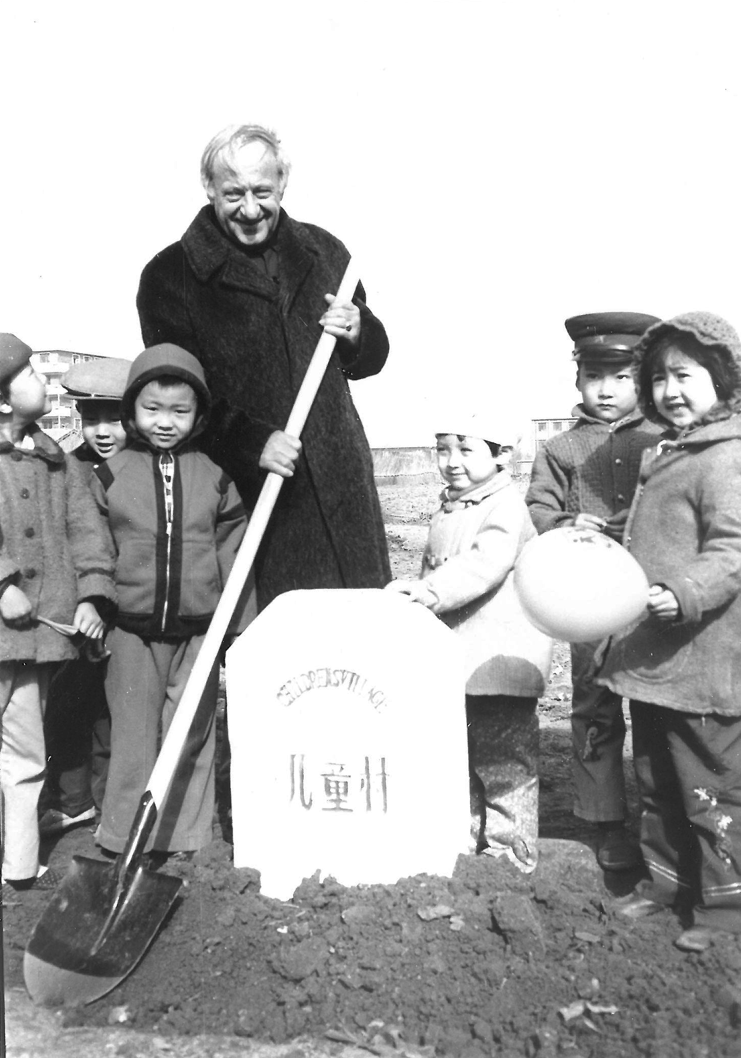Einige Kinder und Hermann Gmeiner mit einer Schaufel in der Hand vor einem Grundstein
