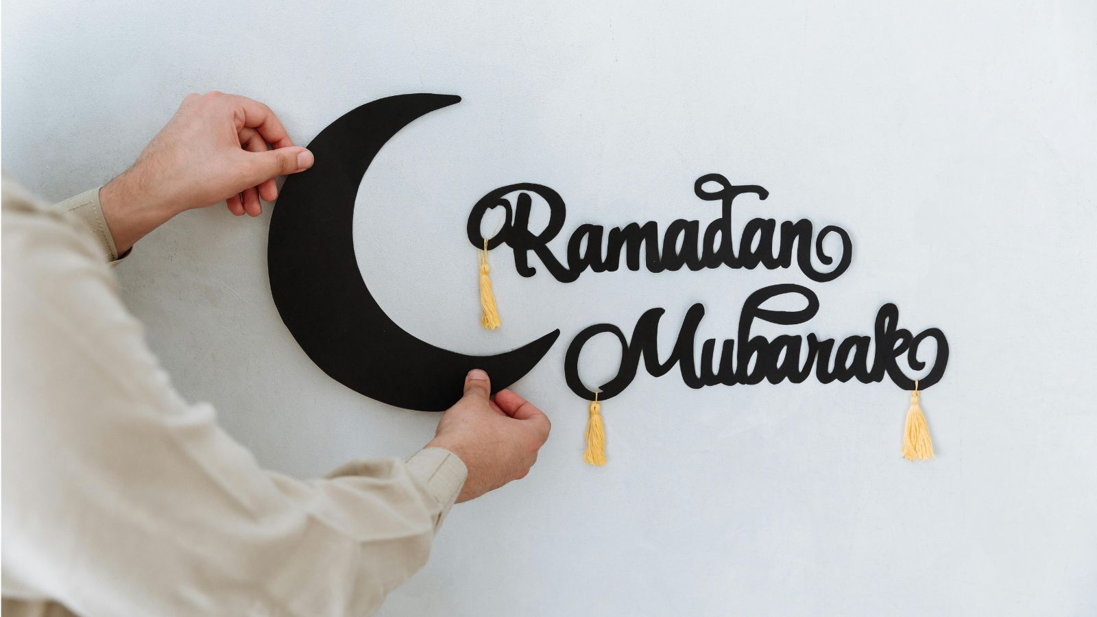 Mann hängt Schriftzug "Ramadan Mubarak" an die Wand, ein Mond ist auch dabei