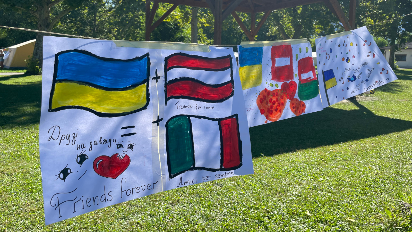 von Kindern gemalte Bilder auf einer Leine aufgehängt, motive: die urainische, österreichische und italienische Flagge und einige Schriftzüge in den jeweiligen Sprachen, "Freunde für immer".
