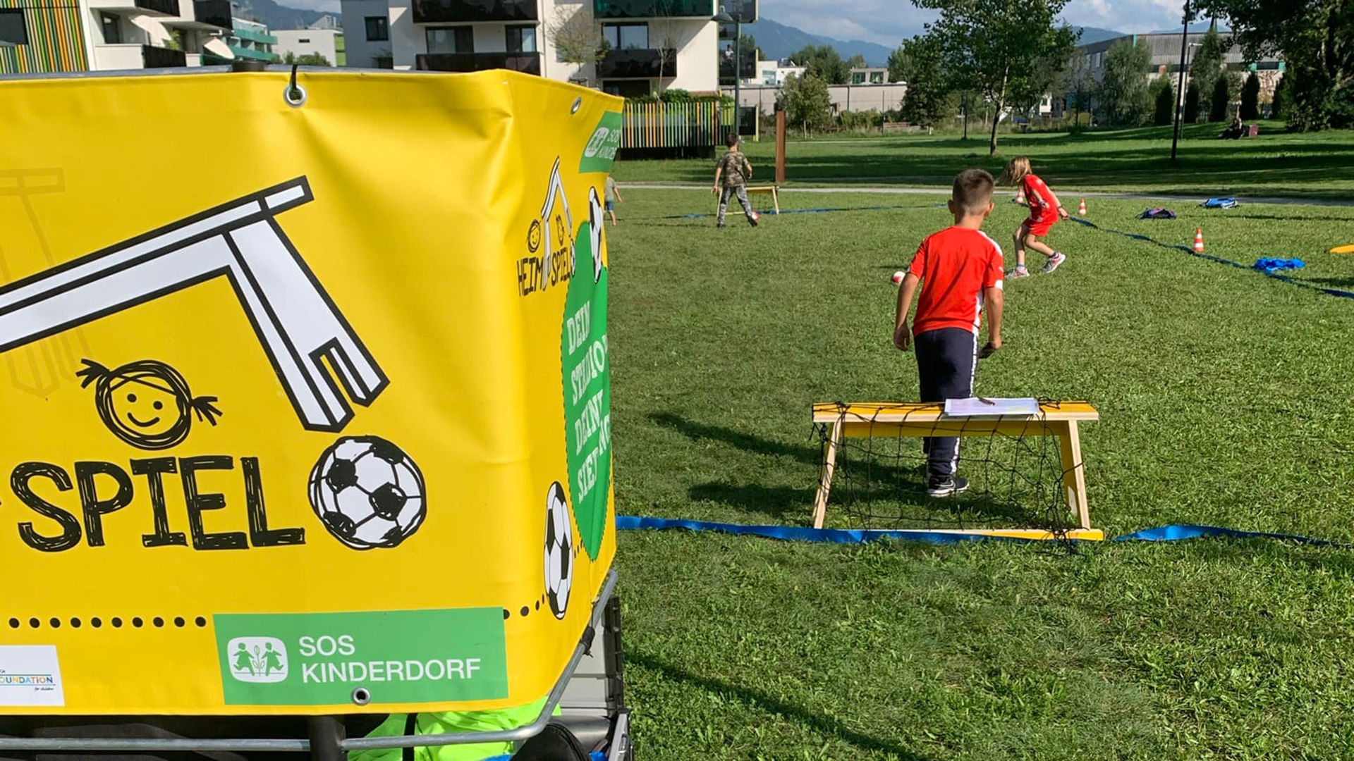 Mobile Mini-Arena im Vordergrund, Kind spielt im Hintergrund Fußball